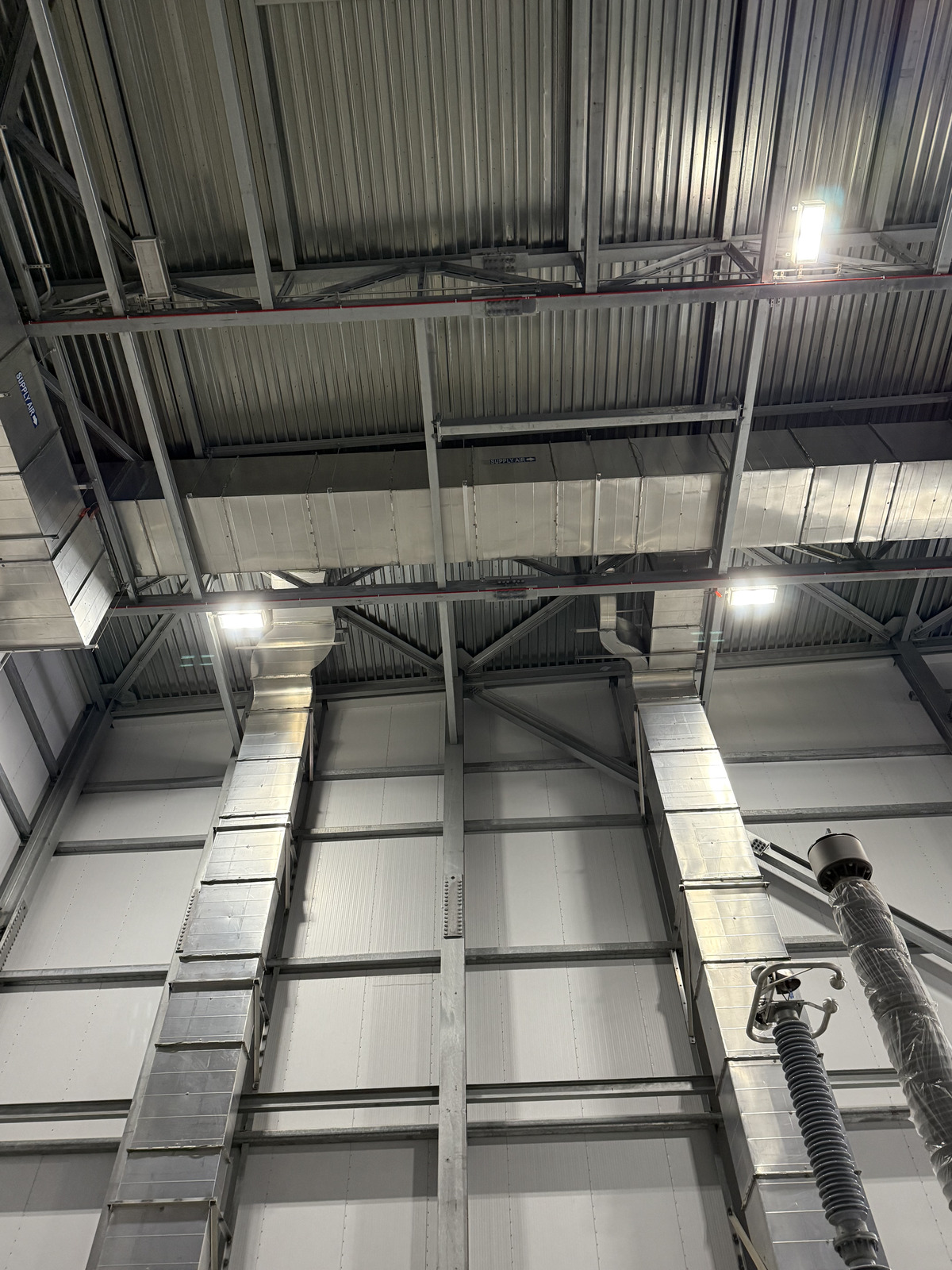 Labeled supply air rectangular duct trunk lines running between steel trusses
