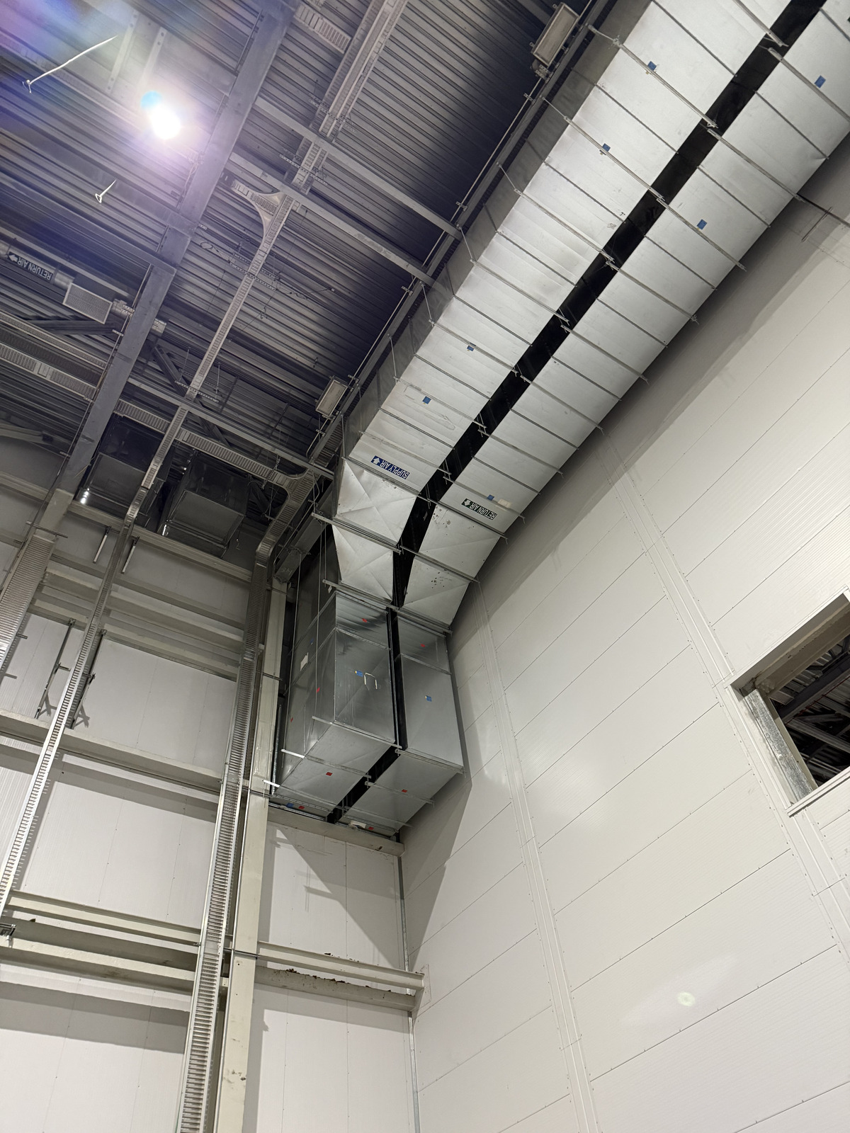 Insulated HVAC duct trunk with a large riser transition along a warehouse wall